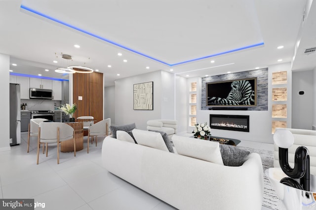 living room featuring recessed lighting, a raised ceiling, a glass covered fireplace, and light tile patterned floors