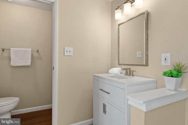 half bathroom with vanity, toilet, wood finished floors, and baseboards