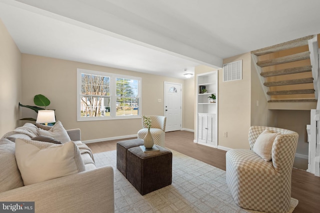 living area with visible vents, baseboards, wood finished floors, and stairway