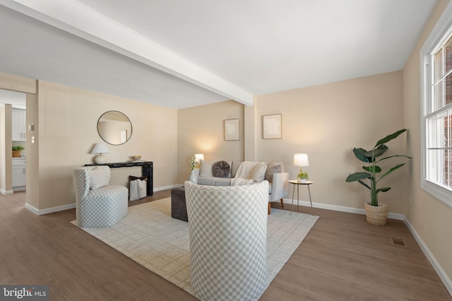 living room featuring visible vents, baseboards, beamed ceiling, and wood finished floors