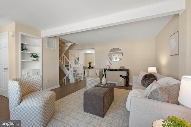 living room featuring built in features, wood finished floors, visible vents, baseboards, and stairs