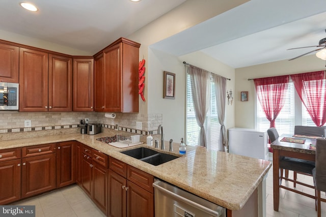 kitchen with light stone counters, stainless steel appliances, a peninsula, a sink, and decorative backsplash