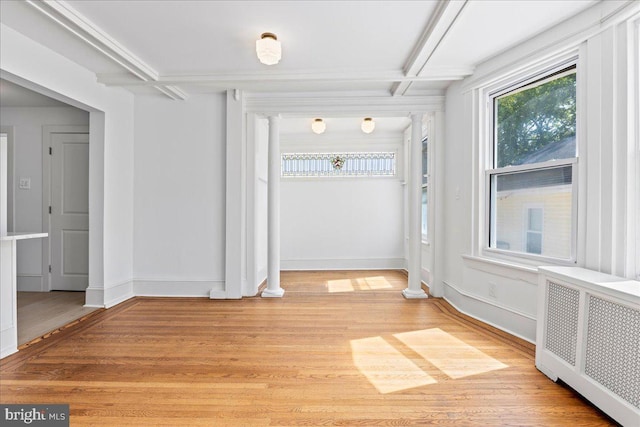 spare room with radiator, light wood-style floors, and beamed ceiling