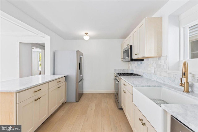 kitchen with light wood-style flooring, appliances with stainless steel finishes, a peninsula, a sink, and backsplash