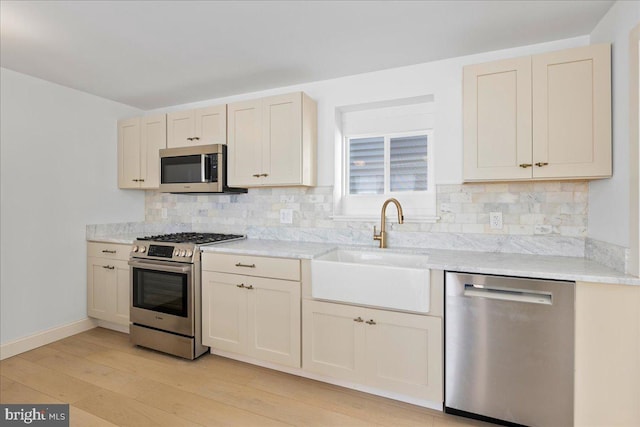 kitchen featuring light wood-style floors, tasteful backsplash, appliances with stainless steel finishes, and a sink