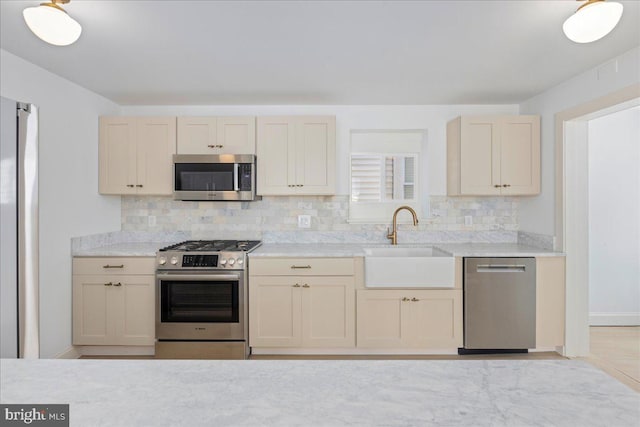 kitchen with appliances with stainless steel finishes, backsplash, a sink, and light stone counters