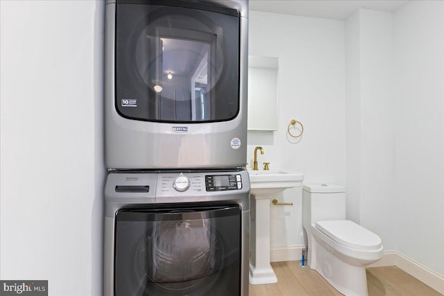 clothes washing area featuring laundry area, a sink, baseboards, light wood-style floors, and stacked washer / drying machine