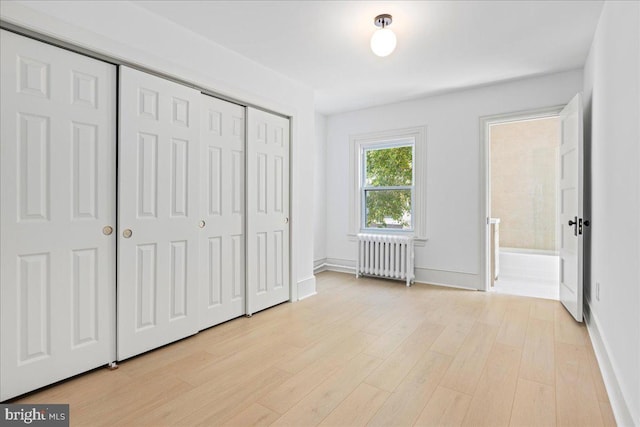 unfurnished bedroom with baseboards, a closet, light wood-type flooring, and radiator