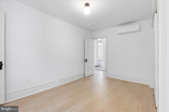 spare room featuring a wall mounted air conditioner, light wood-style flooring, and baseboards