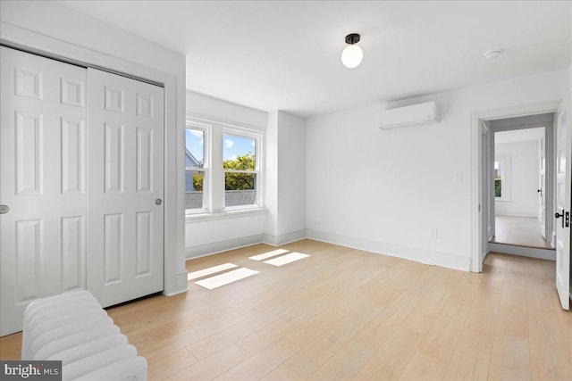 bedroom with light wood finished floors, a wall mounted AC, a closet, and baseboards