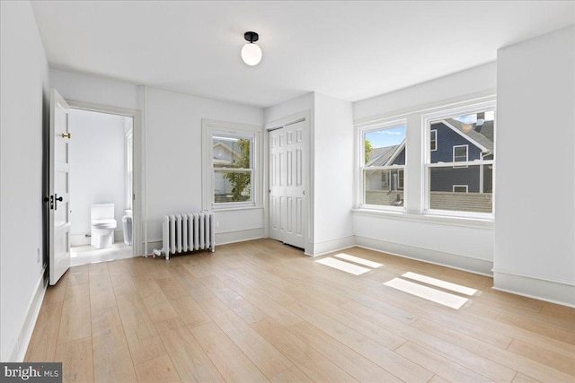 unfurnished bedroom with a closet, light wood-type flooring, radiator, and baseboards