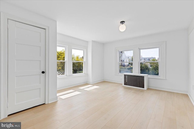 empty room with radiator, light wood-style flooring, and baseboards