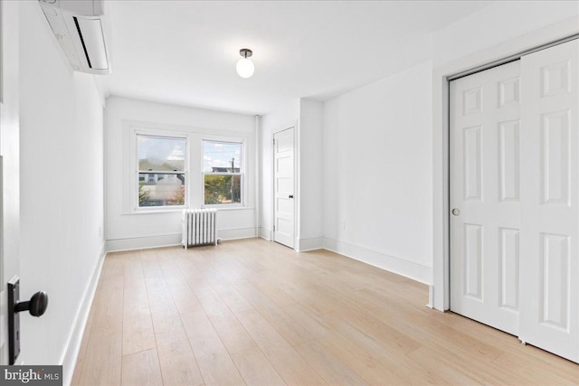 unfurnished bedroom with light wood-type flooring, baseboards, a wall unit AC, and radiator heating unit