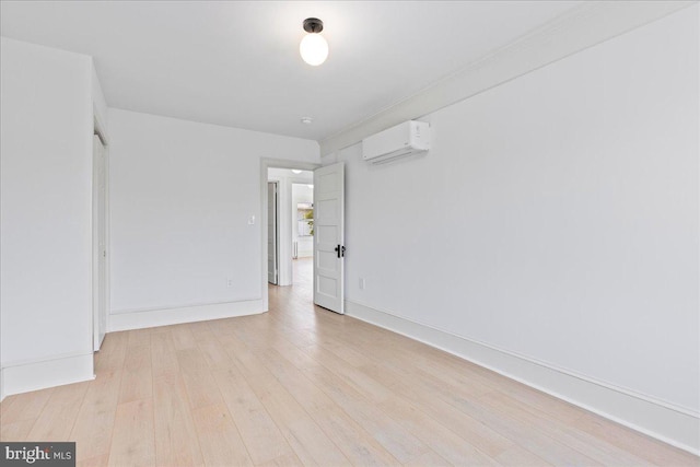 empty room with light wood finished floors, a wall mounted air conditioner, and baseboards