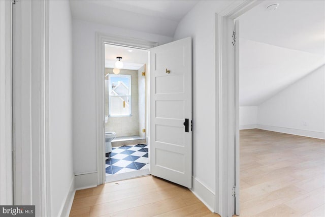 hallway featuring vaulted ceiling, baseboards, and wood finished floors