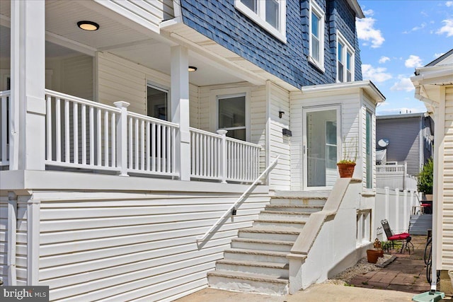 doorway to property with covered porch, mansard roof, and roof with shingles