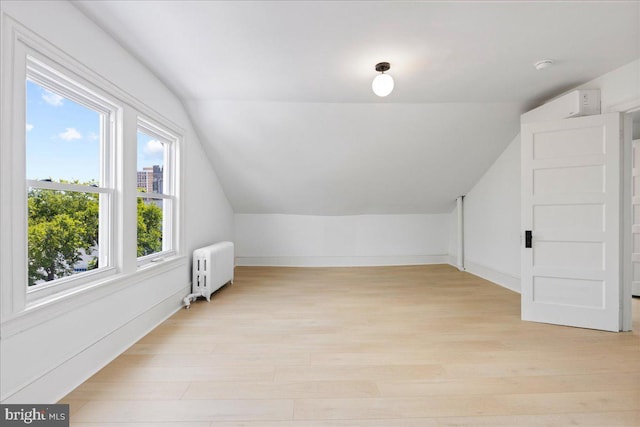 additional living space featuring lofted ceiling, radiator heating unit, and light wood-style floors