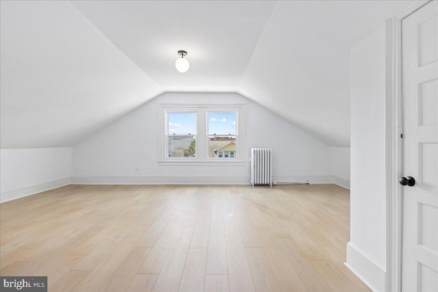 additional living space with lofted ceiling, baseboards, light wood-style flooring, and radiator heating unit