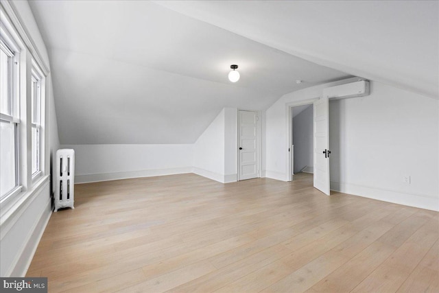 additional living space featuring vaulted ceiling, light wood finished floors, radiator heating unit, and baseboards