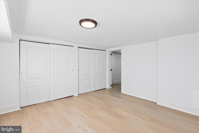 unfurnished bedroom featuring multiple closets, light wood-style flooring, and baseboards