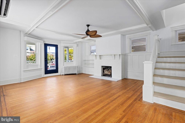 unfurnished living room featuring radiator heating unit, ceiling fan, stairway, light wood-type flooring, and a fireplace