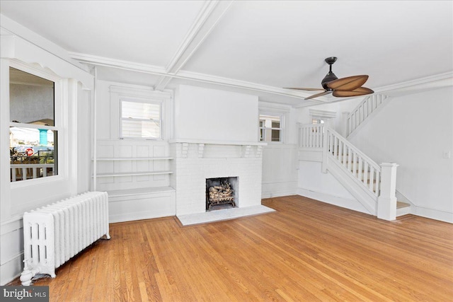 unfurnished living room with radiator, ceiling fan, wood finished floors, stairs, and a brick fireplace