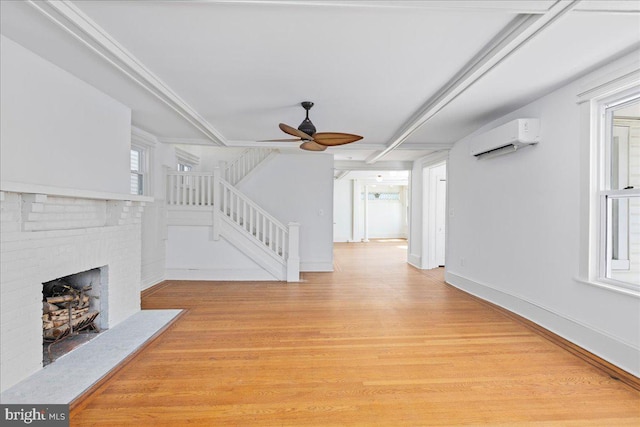 unfurnished living room with a wall unit AC, light wood-style flooring, ceiling fan, stairway, and a fireplace