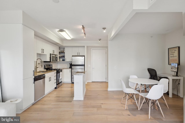 kitchen with light wood finished floors, open shelves, stainless steel appliances, tasteful backsplash, and a sink