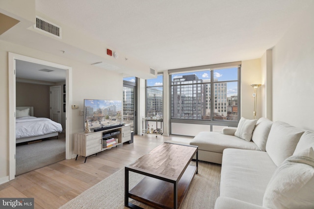 living room featuring light wood finished floors, a wall of windows, and visible vents