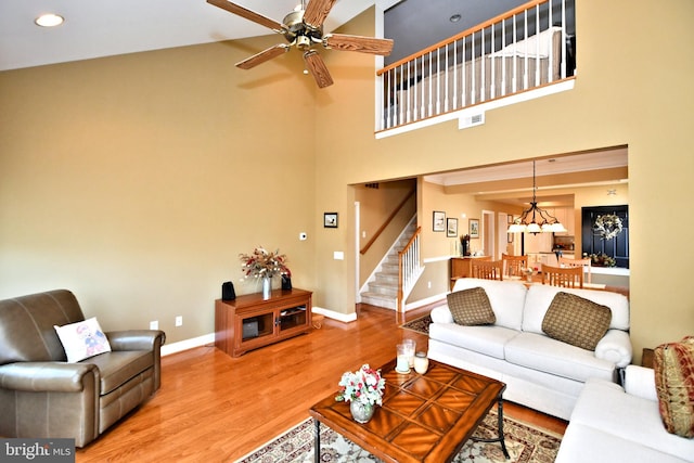 living room featuring a high ceiling, visible vents, baseboards, stairway, and light wood finished floors