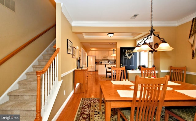 dining space featuring a tray ceiling, light wood-style flooring, visible vents, and crown molding