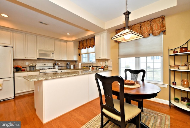 kitchen featuring a tray ceiling, light wood finished floors, decorative backsplash, white cabinets, and white appliances