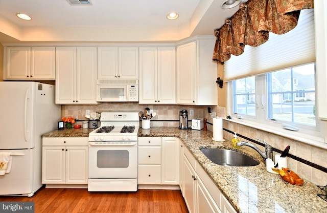 kitchen featuring light wood-style flooring, decorative backsplash, white cabinets, a sink, and white appliances