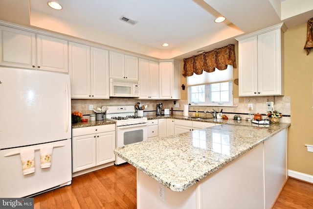 kitchen featuring white appliances, visible vents, a peninsula, and light wood finished floors