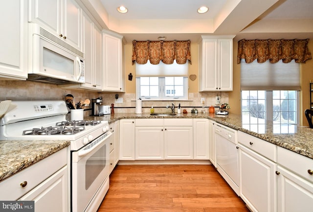 kitchen featuring a tray ceiling, white cabinets, a sink, light wood-type flooring, and white appliances