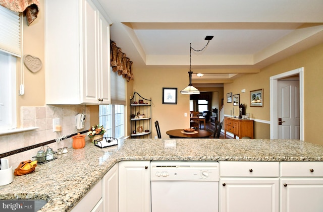 kitchen featuring white dishwasher, a peninsula, white cabinets, backsplash, and a tray ceiling