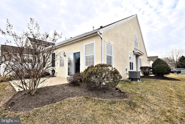 rear view of property with a yard, central AC unit, a patio area, and stucco siding