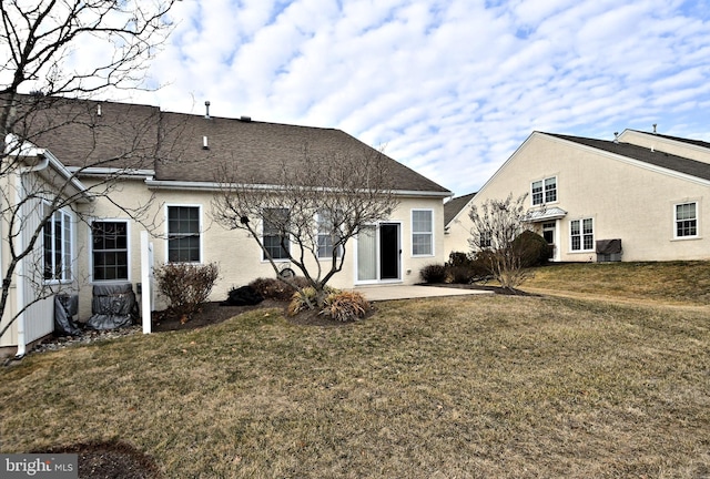 rear view of house with stucco siding, a shingled roof, a lawn, a patio area, and central AC