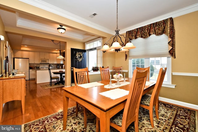 dining area with visible vents, a raised ceiling, wood finished floors, crown molding, and a notable chandelier