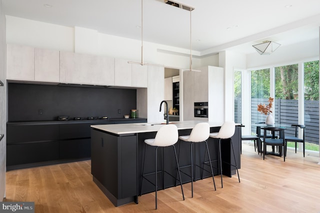 kitchen featuring a breakfast bar area, tasteful backsplash, light countertops, modern cabinets, and light wood-type flooring