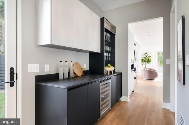 bar with visible vents, wine cooler, light wood-style flooring, and baseboards