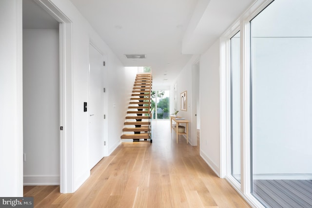 hallway featuring stairs, light wood-style flooring, visible vents, and baseboards