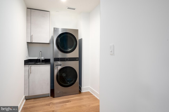 washroom with a sink, baseboards, light wood-type flooring, cabinet space, and stacked washer and clothes dryer