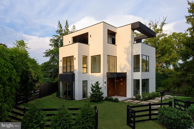 exterior space with a balcony, fence, a front lawn, and stucco siding