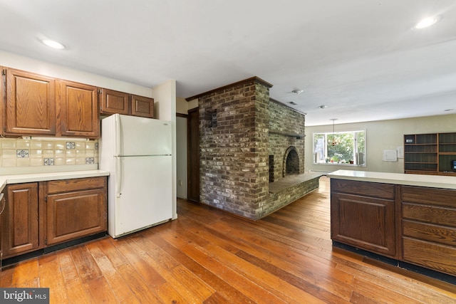 kitchen with tasteful backsplash, hardwood / wood-style floors, freestanding refrigerator, light countertops, and a fireplace