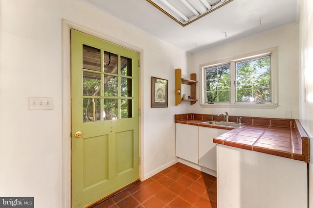 kitchen with ornamental molding, dark tile patterned flooring, a sink, and tile countertops