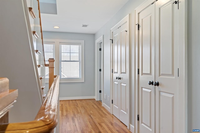 hallway with light wood-style floors, baseboards, stairway, and visible vents