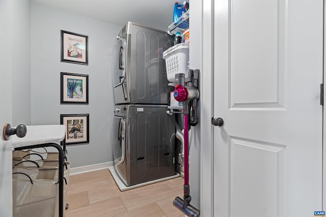 laundry area with laundry area, light wood-style flooring, baseboards, and stacked washer / drying machine