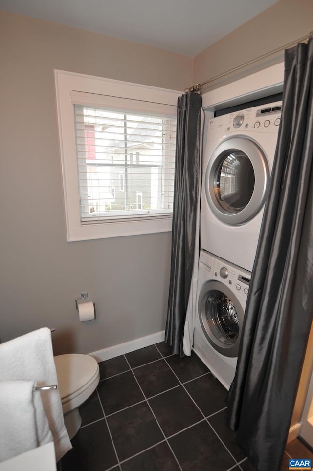 laundry area featuring laundry area, dark tile patterned floors, stacked washing maching and dryer, and baseboards