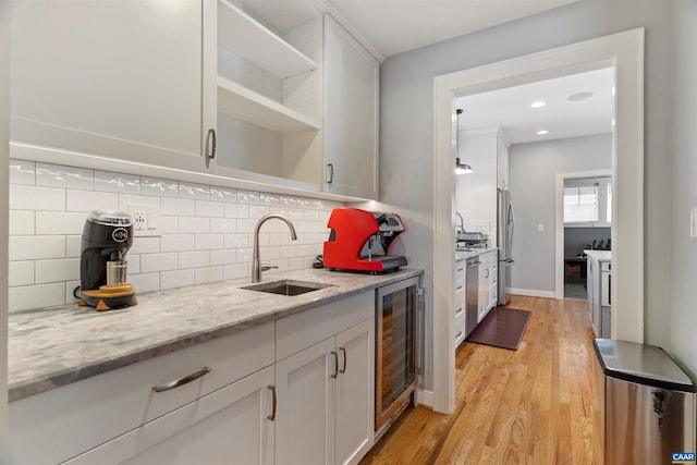 kitchen featuring wine cooler, light wood finished floors, open shelves, freestanding refrigerator, and a sink